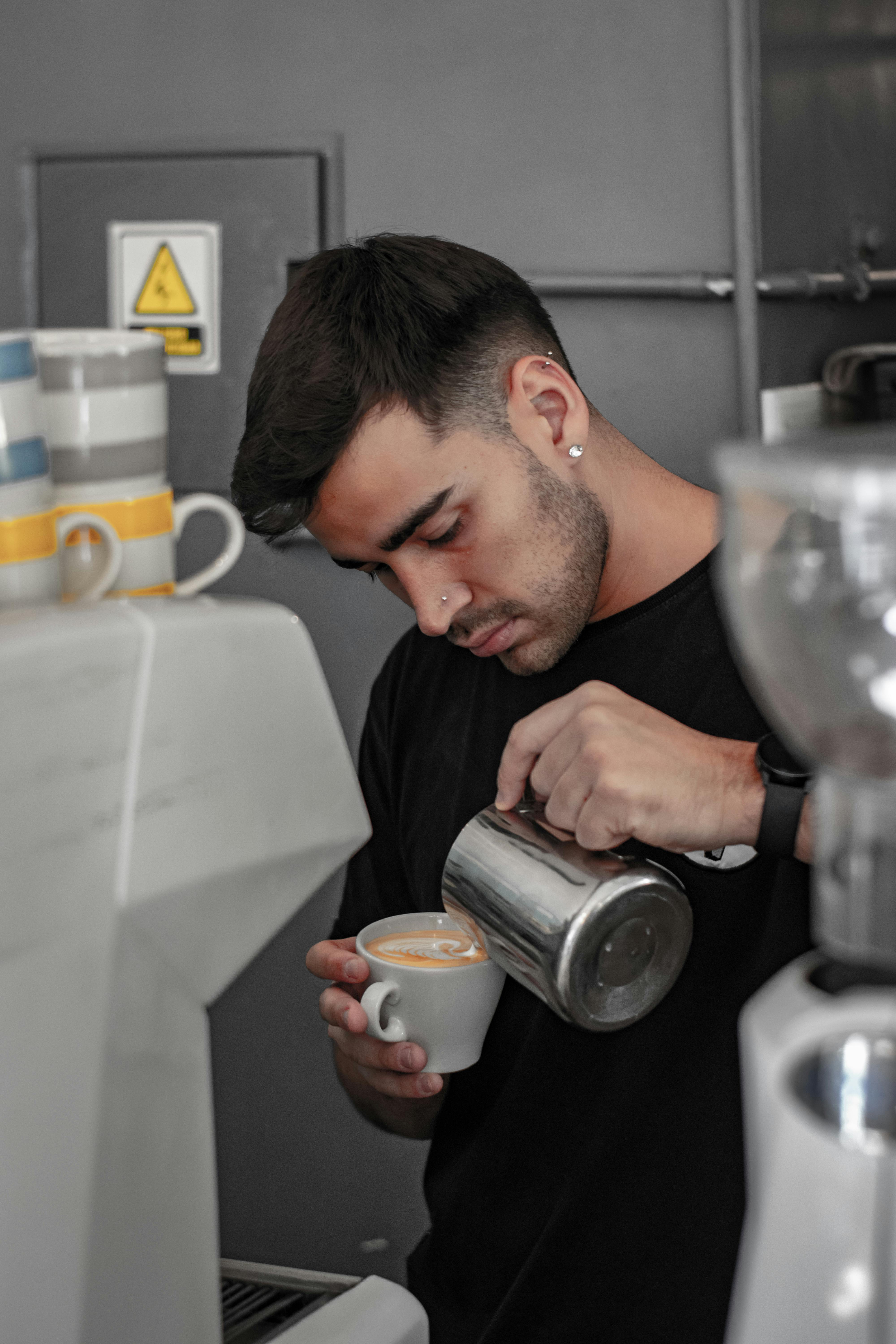 Barista da cafeteria Cantinho do Café utilizando uma ferramenta de latte art para criar um desenho na espuma de leite de um café macchiato artesanal.
